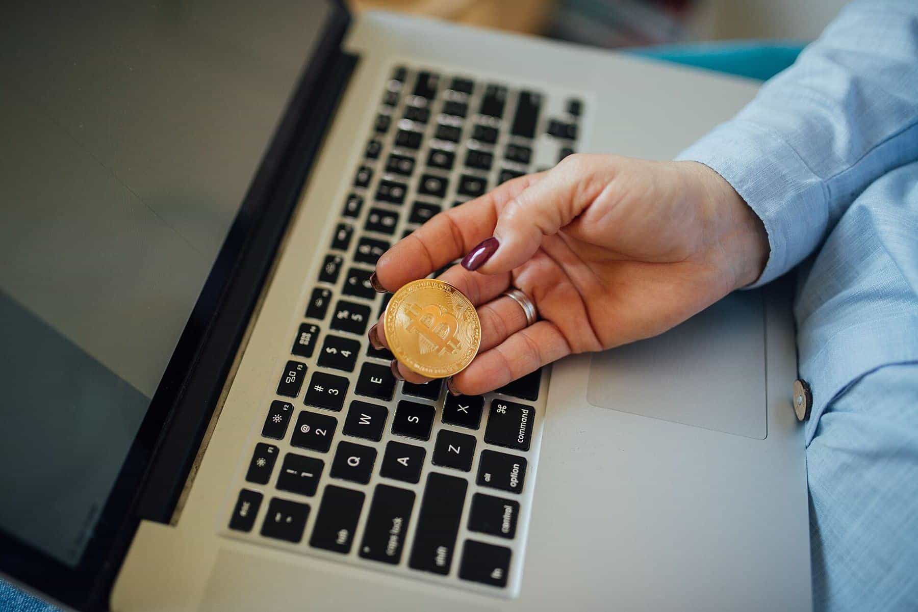 A woman holding a gold-coloured physical bitcoin token above a laptop keyboard
