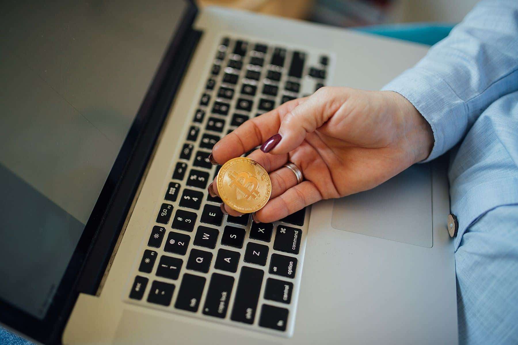 A woman holding a physical bitcoin token above a laptop keyboard