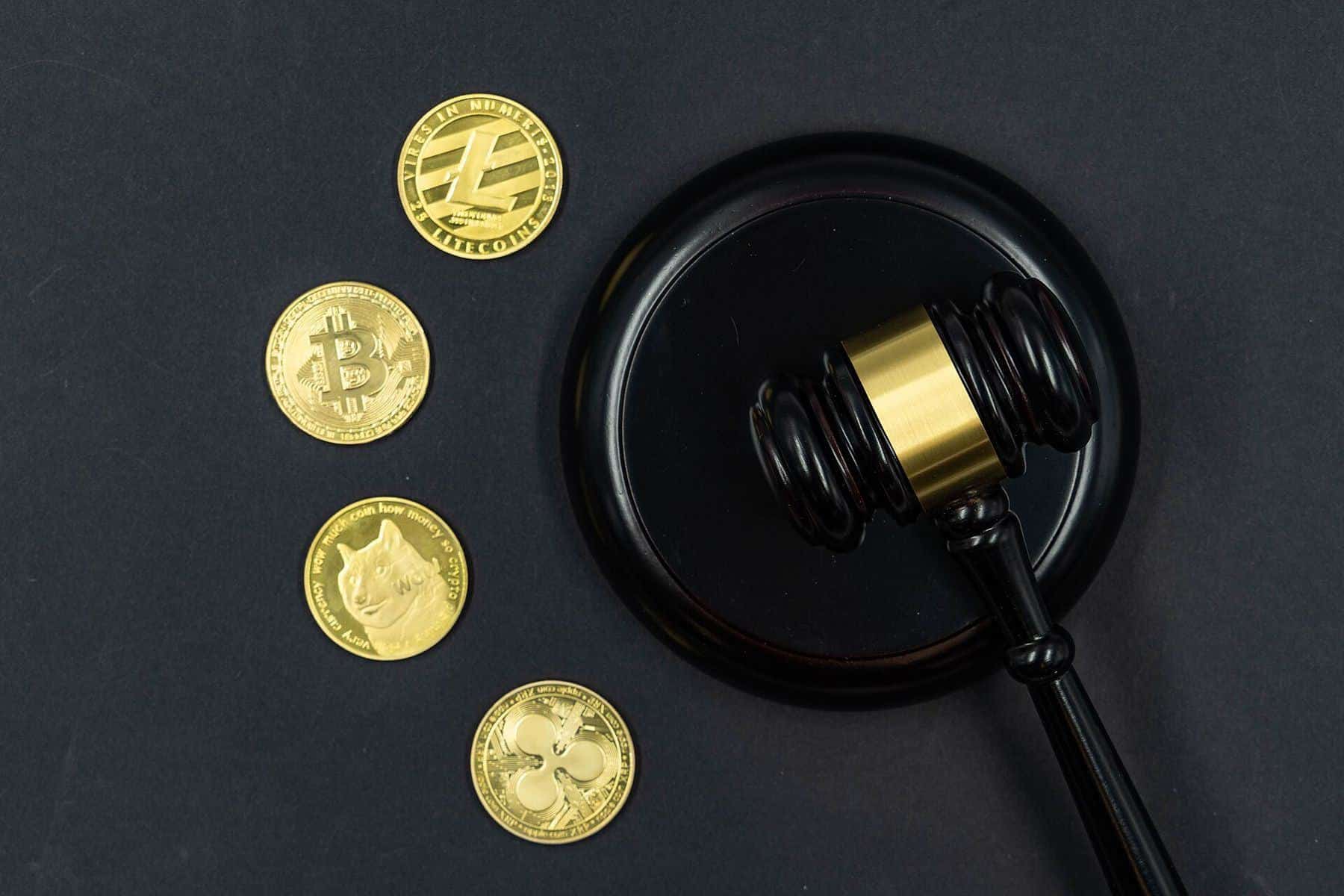 Gold-coloured crypto coins beside a judge's gavel on a dark surface