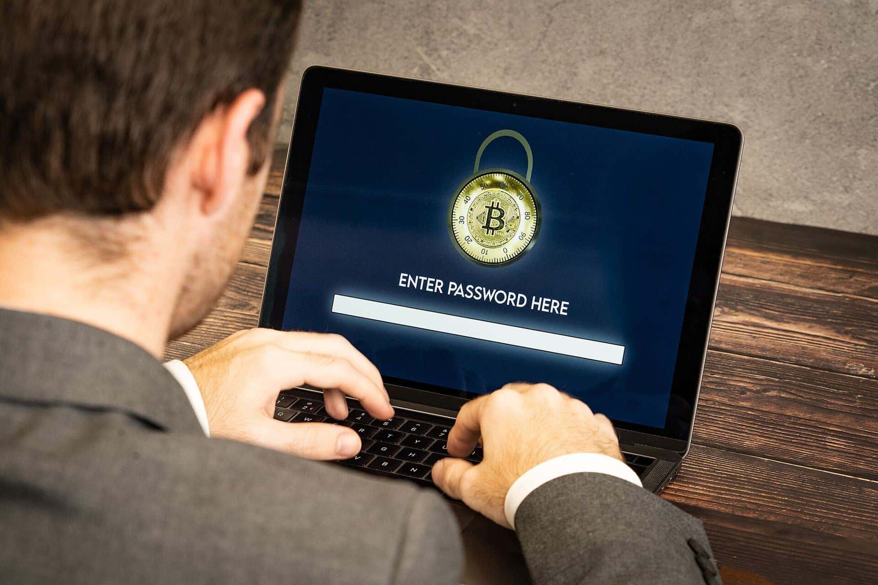 A man in a suit typing a password into a laptop showing a padlock and bitcoin symbol