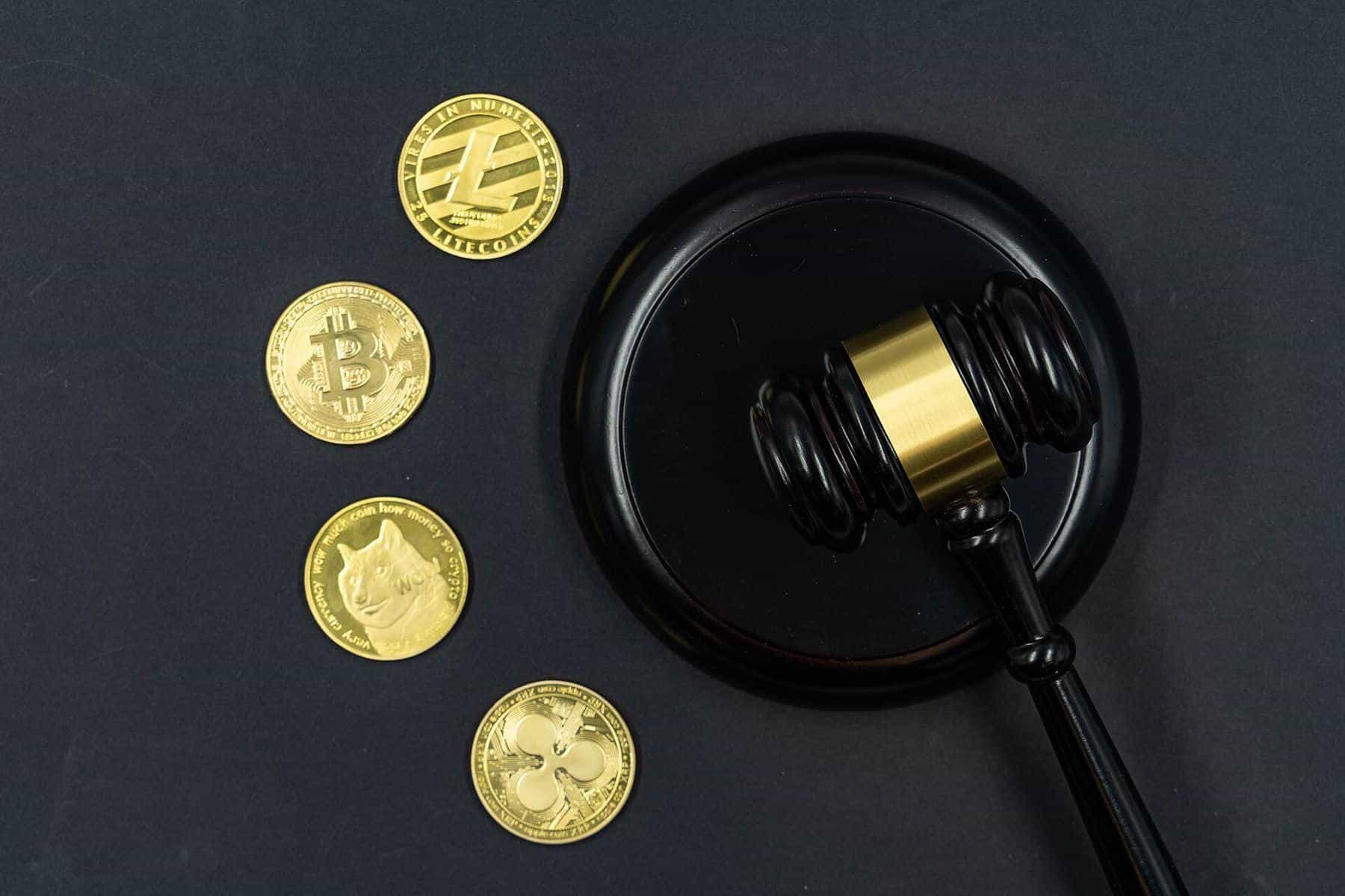 Gold-coloured crypto coins beside a judge's gavel on a dark surface
